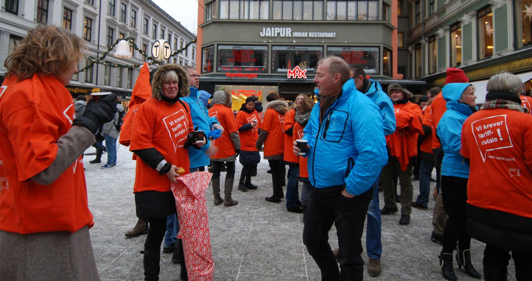 Mennesker med orane tskjorter med påskriften Vi krever tariffavtale er samlet på Egertorget i Oslo