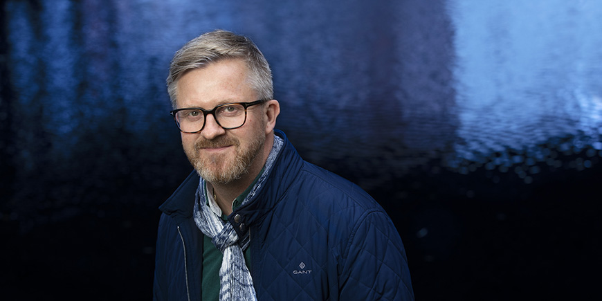 Portrett av Hans-Erik Skjæggerud med blått vann bak.